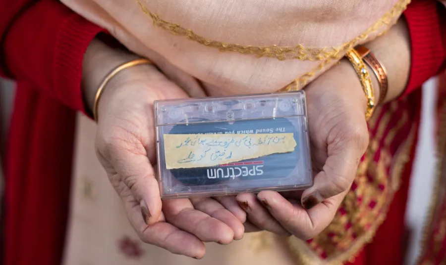 A woman's hands holding a cassette tape. She has bangles on her wrists and is wearing a red cardigan.