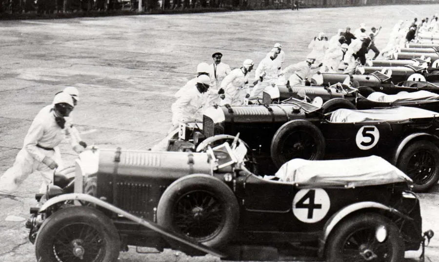 Cars ready to race at Brooklands in 1930 with the Vickers aircraft factory in the background