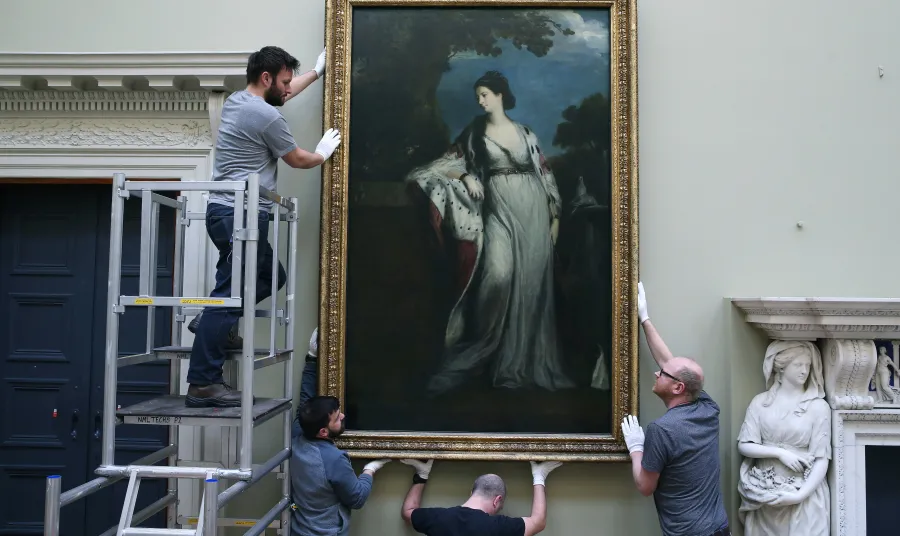 Workmen installing a painting by Sir Joshua Reynolds in the newly restored galleries
