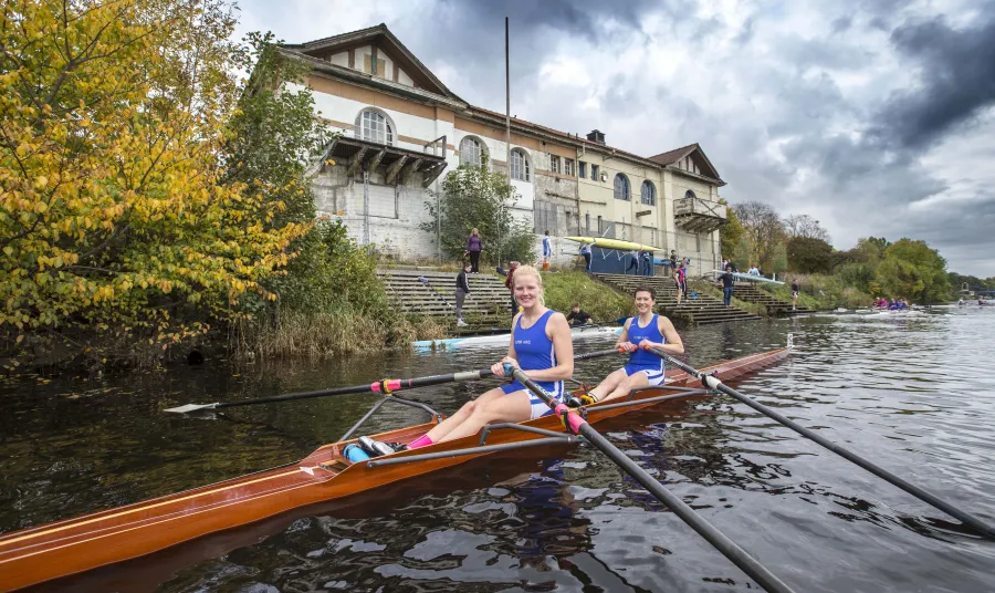 Polly Swann and Caitie Gorton-Phillips in a boat in front of the boathouse