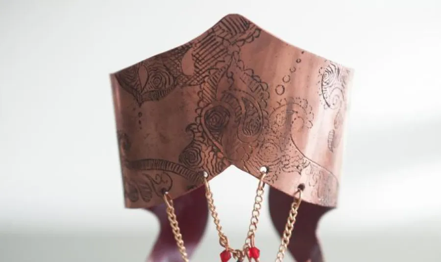 Handmade gold jewellery with red and green gemstones displayed on an intricately carved stand