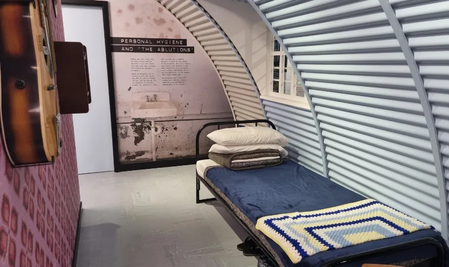 A reconstructed prison cell inside a Nissen hut containing a bed and a guitar