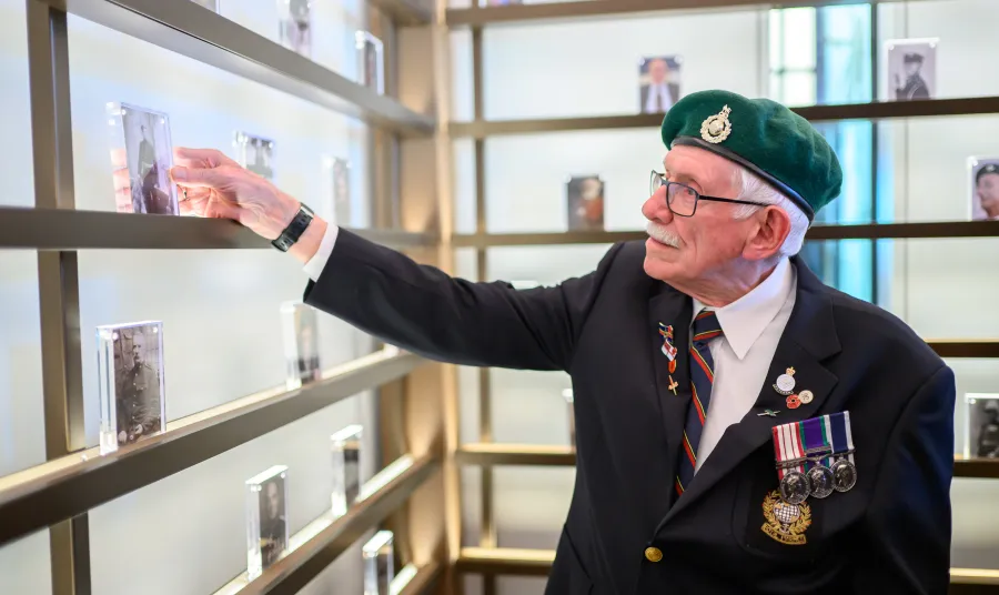 A vetaran wearing a green beret looks at black and white photographs of people in an exhibition space