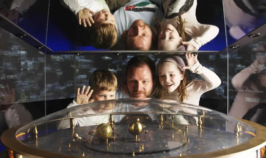 A man and two children look at a machine of an Earth spinning around the sun at the Royal Observatory Greenwich