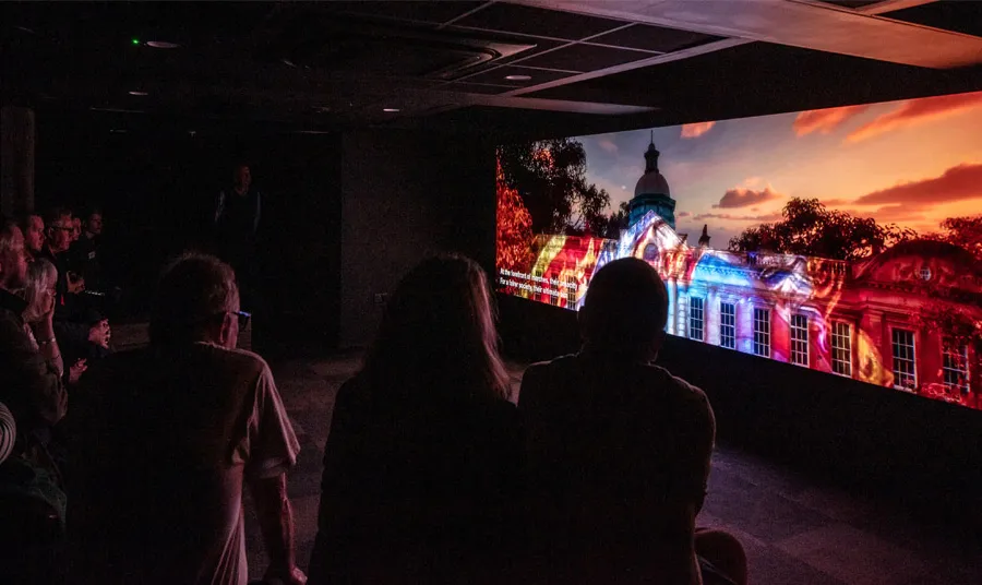 People sit in a dark cinema room watching a film showing the Redhills building illuminated with a colourful light projection