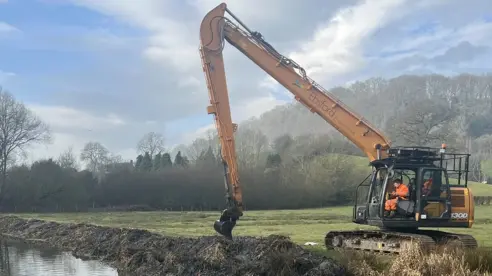 A digger clearing a section of the canal in an area with hills, trees and fields