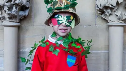 A child in a red jumper, hat and eye mask draped in ivy