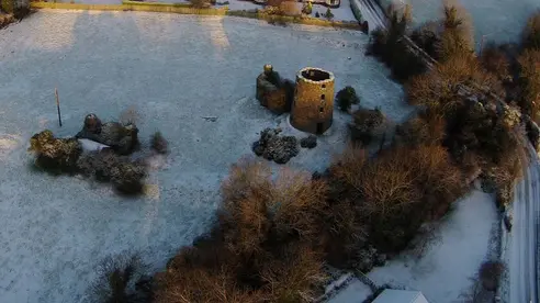 An aerial photo of a field with ruined mill buildings during winter