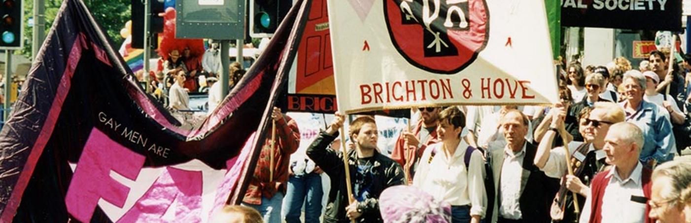 Brighton Pride, 1995: Pobl yn gorymdeithio i lawr stryd yn dal baneri sefydliadau sy'n cefnogi pobl LHDTC+