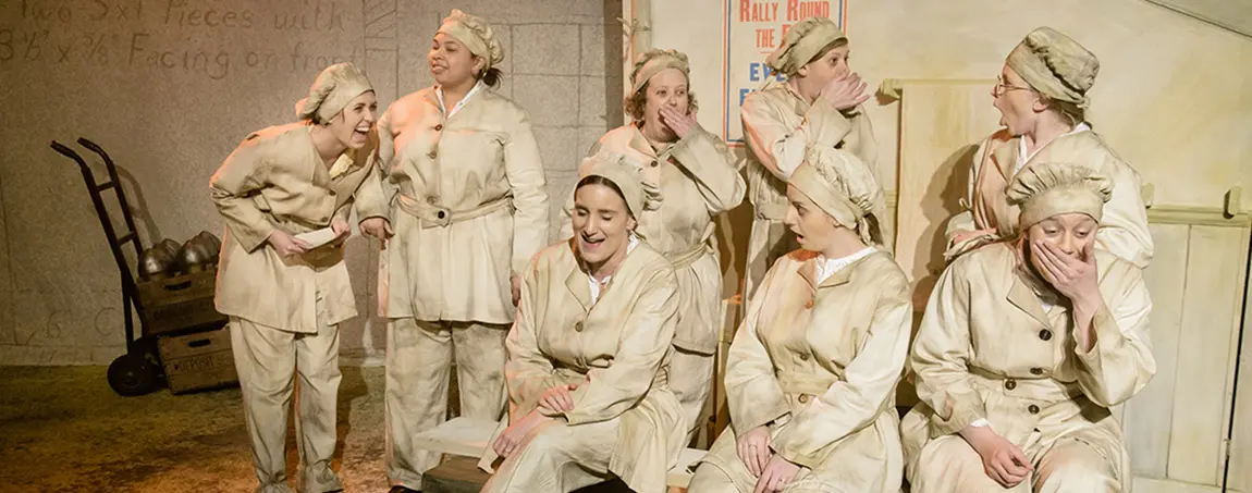 People dressed up as Gas girls from World War I. Some are sitting and others are standing behind them, laughing and gasping