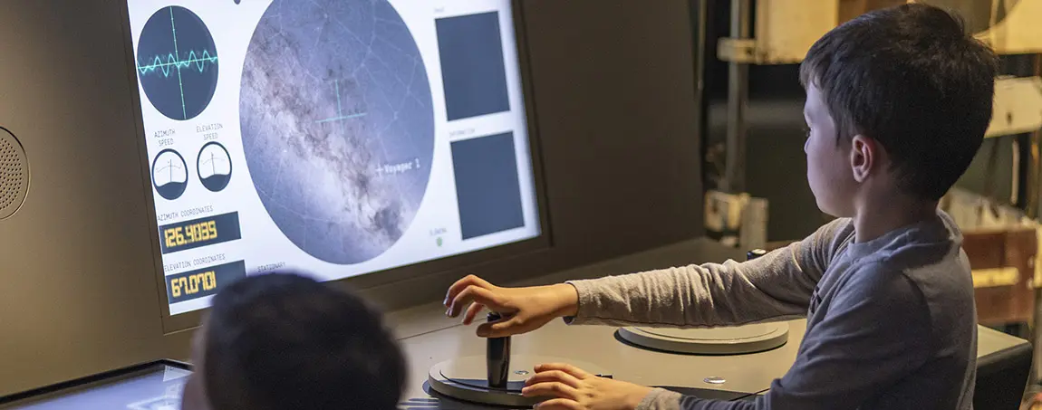 Two children interacting with a screen at the First Light Pavilion exhibition, Jodrell Bank.