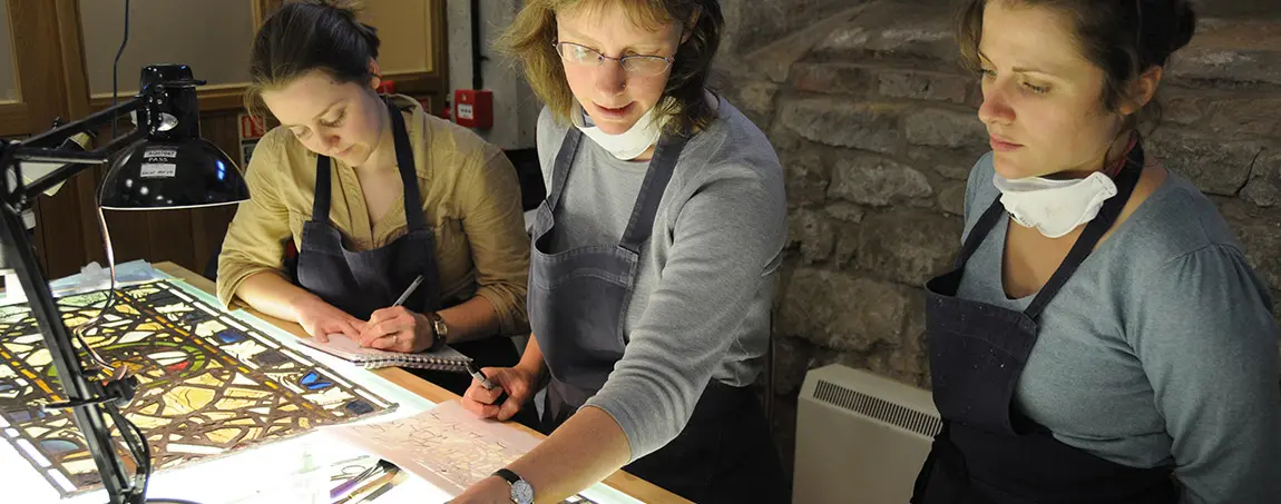 Three people doing conservation work on a stained glass window on a table