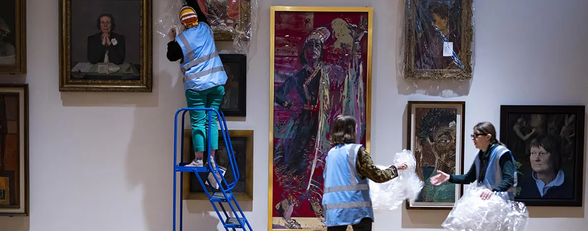 Three people hanging paintings on a wall using a step ladder