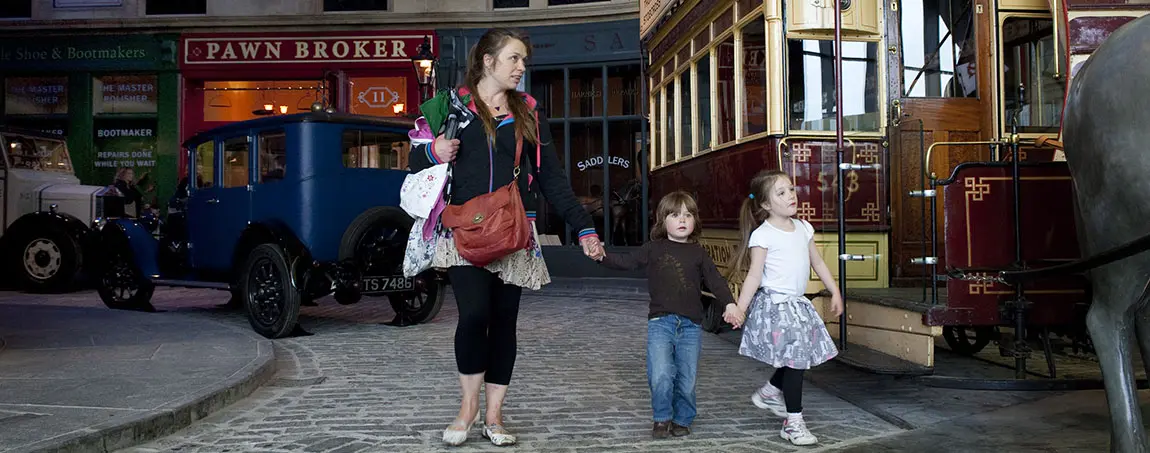 An adult and two children look at a tram in a museum recreating a historic street