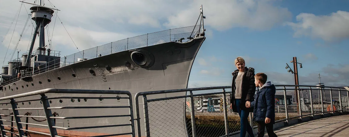 An adult and a child looking at a First World War era ship in a dock