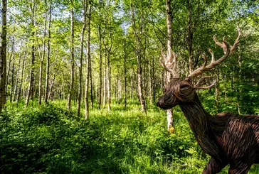 A deer sculpture is situated amongst trees