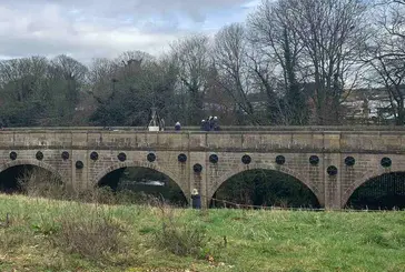 Figures abseiling off a viaduct, with surrounding trees and grass