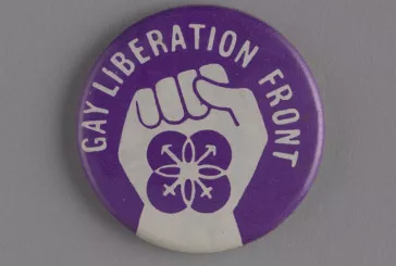 A purple pin badge with a white fist outline that reads gay liberation front 