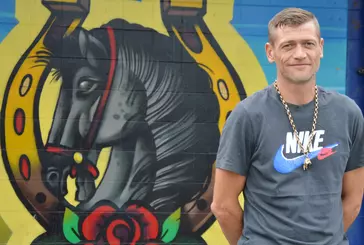 Person smiles at camera, standing in front of artwork showing a horse