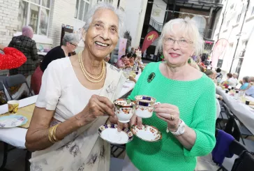 Two people smiling whilst holding cups of tea