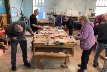 People stand around a workbench using tools
