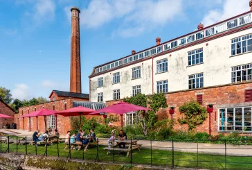 People sitting on benches outside historic building next to the river on a sunny day