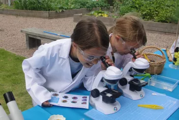 Two children wearing white science coats looking into microscopes