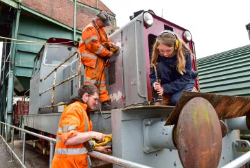 Three people dressed in high visibility vests work on stationary heritage train