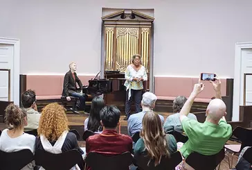 A black performer stands in front of a small audience, giving a workshop