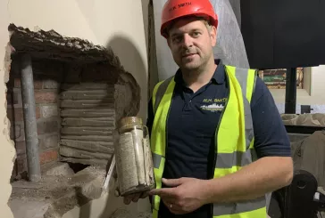 Man wearing a hard hat holding a capsule, standing next to a hole in the wall