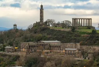 A skyline view of Calton Hill in Edinburgh. In the foreground, the Royal High School stands on the steep banks of the hill. At the summit, the Nelson Monument and the National Monument for Scotland stand tall against the sky.