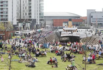 Hundreds of people are gathered, enjoying the sunshine, around a historic ship in dry dock on the Belfast quayside.