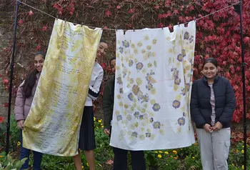 People standing behind a textile artwork made from hanging sheets of fabric printed with text and flowers