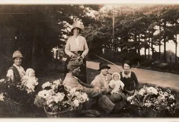 A historic black and white photograph of a group of Traveller people with infants selling flowers