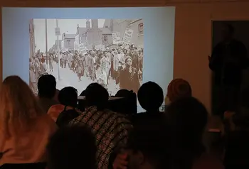 A group of people sit in a dark room watching a projection with images of a protest