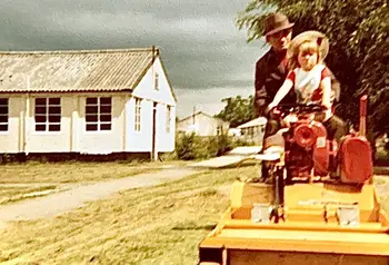 An old photograph of an adult and a child on a ride-on lawnmower
