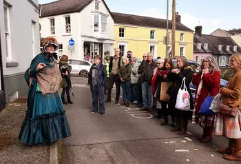 A person in historical dress stands in a street and talks to a tour group