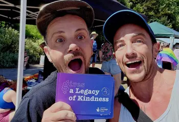 Two people at an outdoor event holding a card saying A Legacy of Kindness