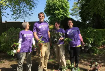 Four people holding plants whilst smiling at camera