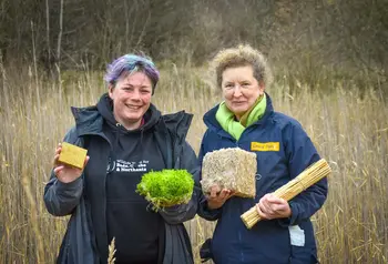 Two people standing in a fen carrying crops that have been turned into insulation products