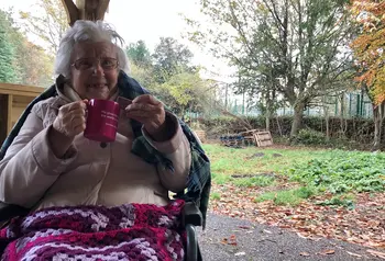 Elderly woman using wheelchair in garden, smiling with tea and biscuit