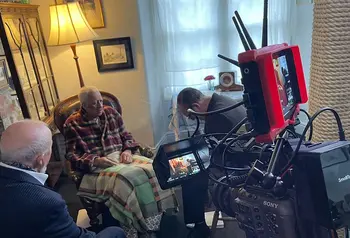 Behind the scenes at a film set: three actors act a scene in a living room while a camera films
