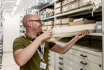a man takes a cloth bag containing a rolled up document off a shelf in an archive
