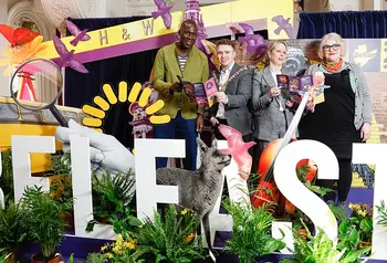Four people pose with leaflets behind large letters spelling 'Belfast' surrounded by foliage and props