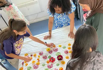 A group of young people arranging flowers and leaves on a white sheet
