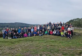 A large group of people wearing outdoor clothing pose for a group photo in the countryside