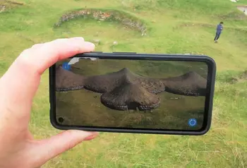 A visitor to Cladh Hallan on Uist uses augmented reality through the camera of their phone to see what the original structures on the site looked like.