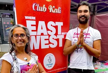 Two south asian people stand next to a banner with text: Club Kali Where East Meets West made possible with Heritage Fund