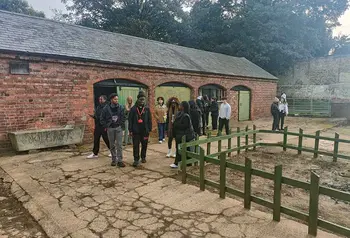 A group of young people stand in front of a red brick stable block