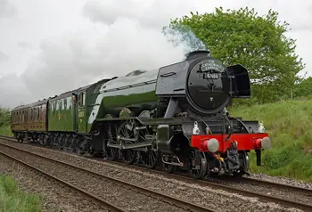The Flying Scotsman, a large dark green steam engine, pulls a heritage service through the countryside.